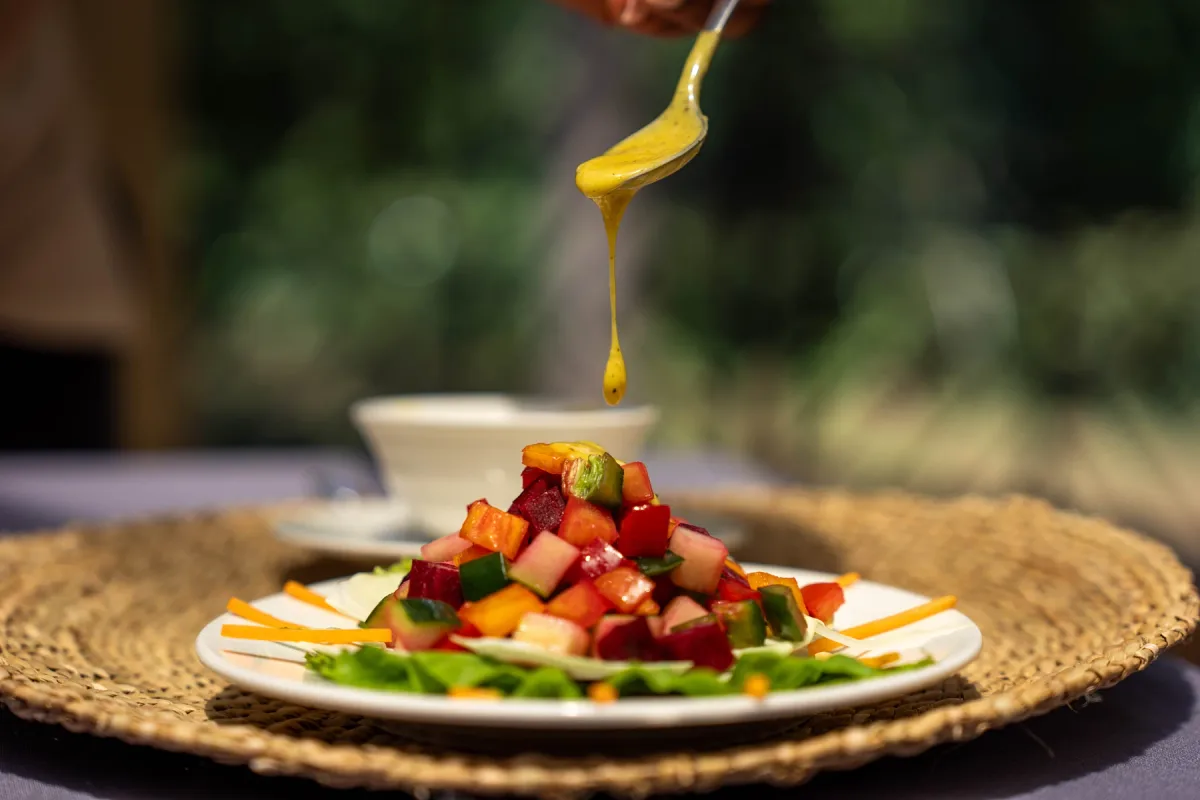 A freshly plated dish being finished with sauce in warm natural light